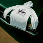 Buzo Porsche GT3 blanco con diseño Candy 911 GT3 RS en la espalda sobre capó de auto clásico.